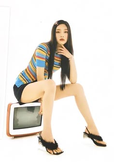 a woman sitting on top of a tv next to a white wall with her legs crossed