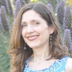 a woman standing in front of purple flowers with her eyes closed and smiling at the camera