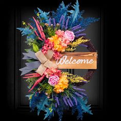 a welcome wreath with flowers and leaves hanging on a door