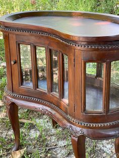 an old wooden cabinet with glass doors on the top and bottom, sitting in grass