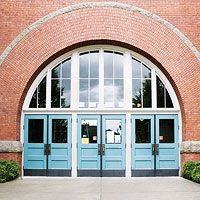 the front entrance to a brick building with two blue doors and arched windows on each side