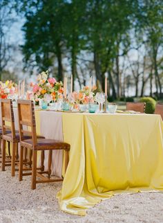 the table is set with yellow linens and flowers on it, along with candles