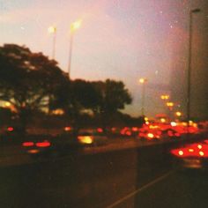 many cars are driving down the road at night time, with lights on and trees in the background