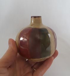 a hand holding a small ceramic vase in it's right hand, with the bottom half painted red and the other half green