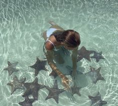 a woman is in the water surrounded by starfish