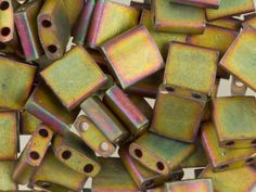 a pile of metallic square beads with holes in them on a white tablecloth background