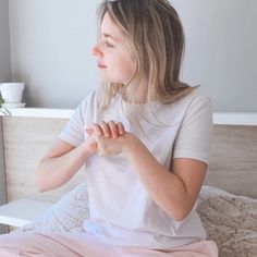 a woman sitting on a bed with her hands clasped