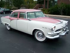 an old pink and white car parked in a parking lot