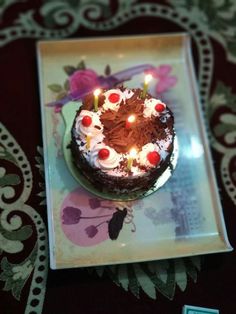 a chocolate cake with white frosting and lit candles on a decorative tableclothed place mat