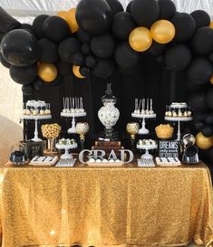 a table topped with lots of black and gold desserts next to a giant balloon