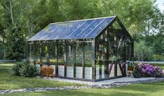 a small greenhouse in the middle of some grass with flowers and plants growing around it