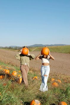 two women walking through a field with pumpkins on their heads