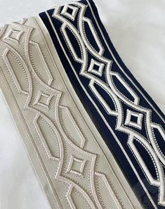 two ties laying next to each other on top of a white bed sheet with an intricate design