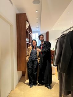 the man and woman are standing next to each other in front of some clothing racks