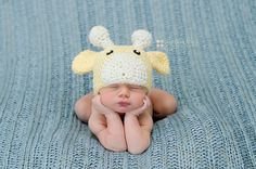 a baby wearing a crocheted giraffe hat laying on top of a blue blanket