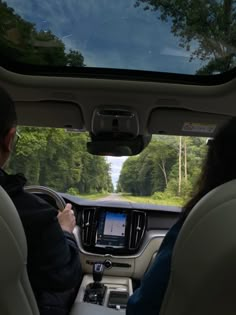 two people in the back seat of a car driving down a road with trees on both sides