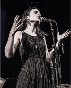 a woman standing in front of a microphone and holding her hands up to the air