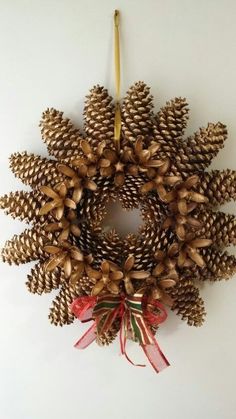 a pine cone wreath hanging on the wall with a candle and ribbon tied around it