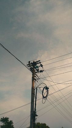 an overhead view of power lines and telephone poles against a cloudy sky with trees in the foreground