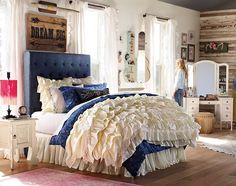 a bed with ruffled sheets and pillows in a bedroom next to a dresser, mirror and window