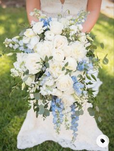 a bride holding a bouquet of white and blue flowers on her wedding day in the grass