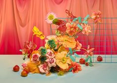 an arrangement of flowers and fruit in front of a red curtained background with pink curtains