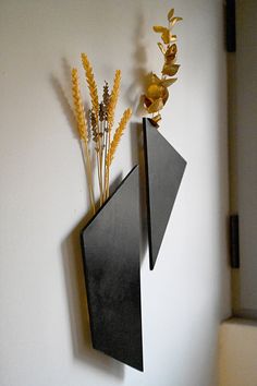 a vase with some flowers in it sitting on a wall next to a black sculpture