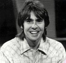 an old black and white photo of a smiling man with long hair wearing a plaid shirt