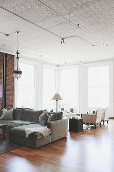 a living room filled with lots of furniture next to tall windows on top of a hard wood floor