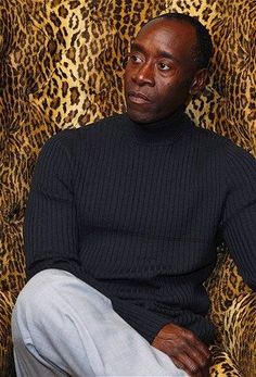 a man is sitting in front of a leopard print wall with his hand on his hip