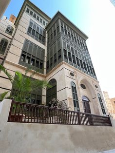 a tall building with lots of windows next to a fence and palm tree in front of it