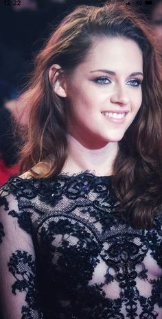 a woman with long hair wearing a black dress and smiling at the camera while standing in front of a red carpet