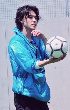 a young man holding a soccer ball in his right hand and wearing a blue jacket