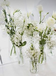 three vases with white flowers in them on a tableclothed cloth, one is empty and the other has small baby's breath