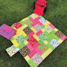 a colorful patchwork quilt laying on the grass next to a red bag and purse