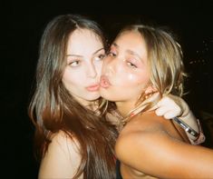 two young women are kissing each other in front of the camera at night, one is blowing out her tongue