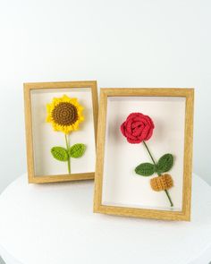 two small crocheted flowers in wooden frames on a white surface with one red and one yellow flower