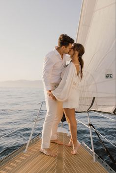 a man and woman kissing on the deck of a sailboat in the ocean with their arms around each other