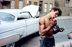 a shirtless man standing in front of a white car next to a fire hydrant