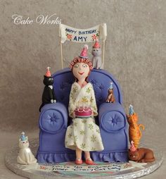 a birthday cake with a woman sitting on a blue chair surrounded by cats and dogs