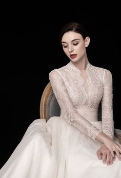 a woman sitting on top of a chair wearing a white dress with sheer sleeves and lace detailing