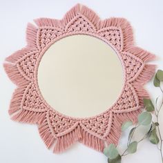 a pink doily with leaves on the side and a round mirror in the middle