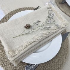 a place setting with napkins and silverware on a white table cloth covered plate