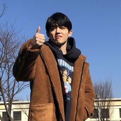 a young man giving the thumbs up while standing in front of a building with trees