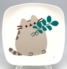 a white plate with a cat holding a green plant on it's back side