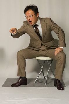 a man in a suit sitting on a chair with his hands out and pointing at something