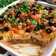 an enchilada dish with black olives, tomatoes, green onions and cheese