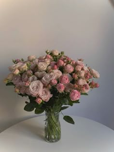 a glass vase filled with pink flowers on top of a white table next to a wall