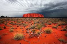 a red rock in the distance under a cloudy sky