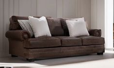 a living room with a brown couch and white pillows on top of it's back